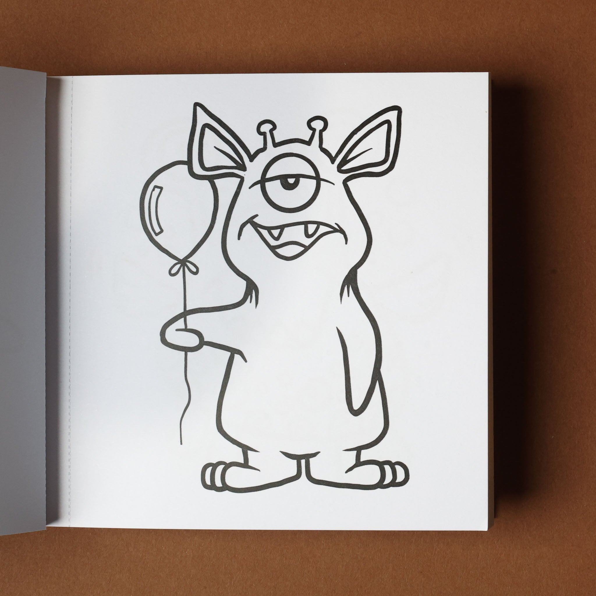 Monster drawing with a balloon on a white sheet of paper, open book on brown background