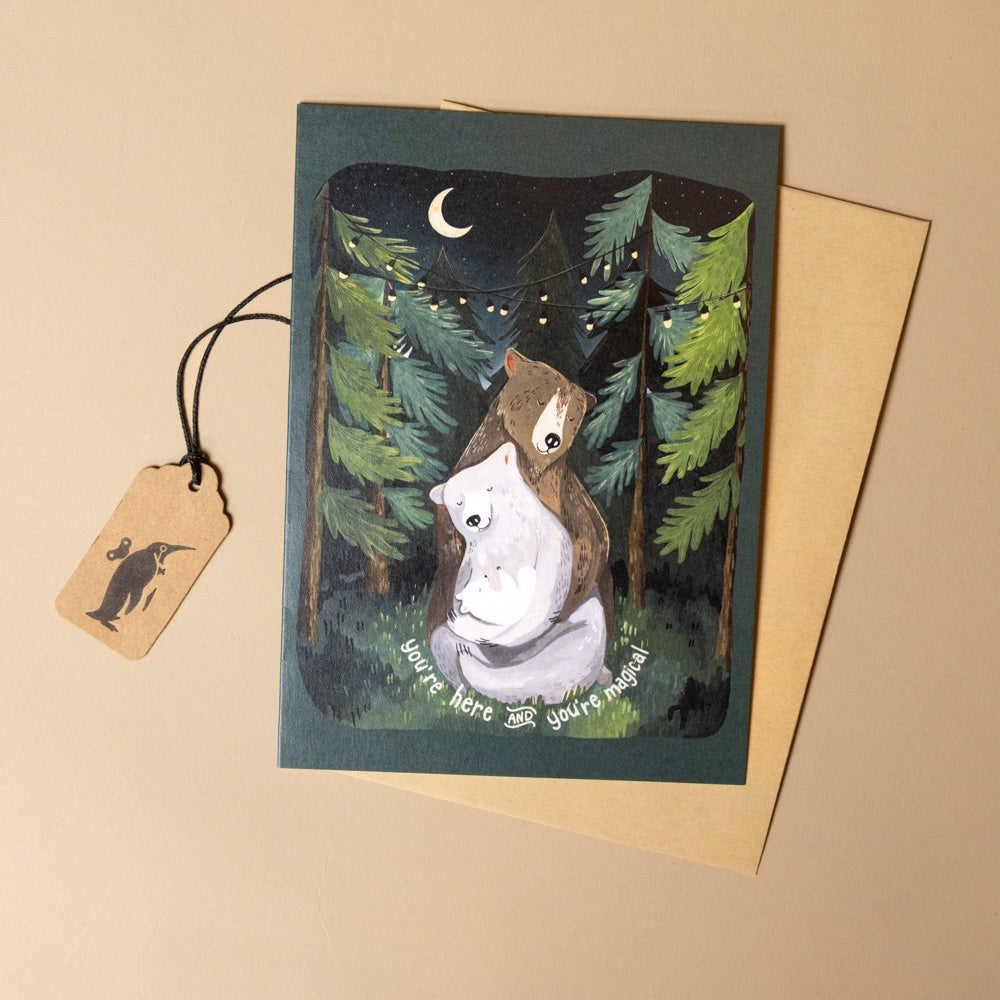 magical-forest-night-greeting-card with illustration of two bears in a forest at night, accompanied by a tag and envelope on a beige background.