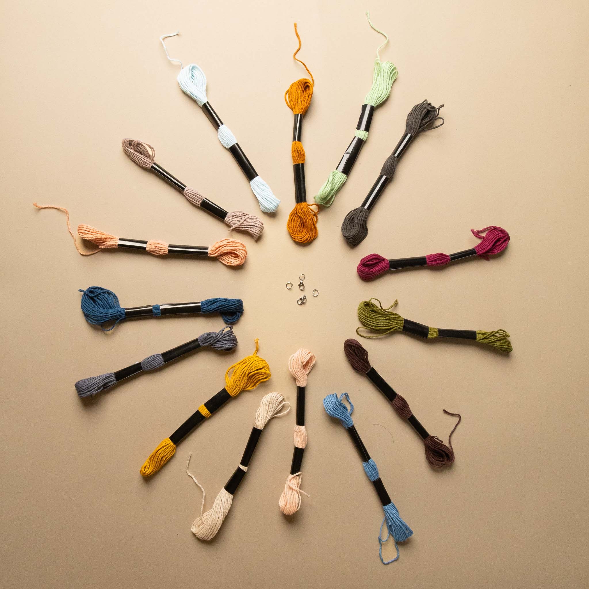make-your-own-friendship-bracelets-kit Assorted skeins of yarn on wooden sticks arranged in a circular pattern on a beige background.