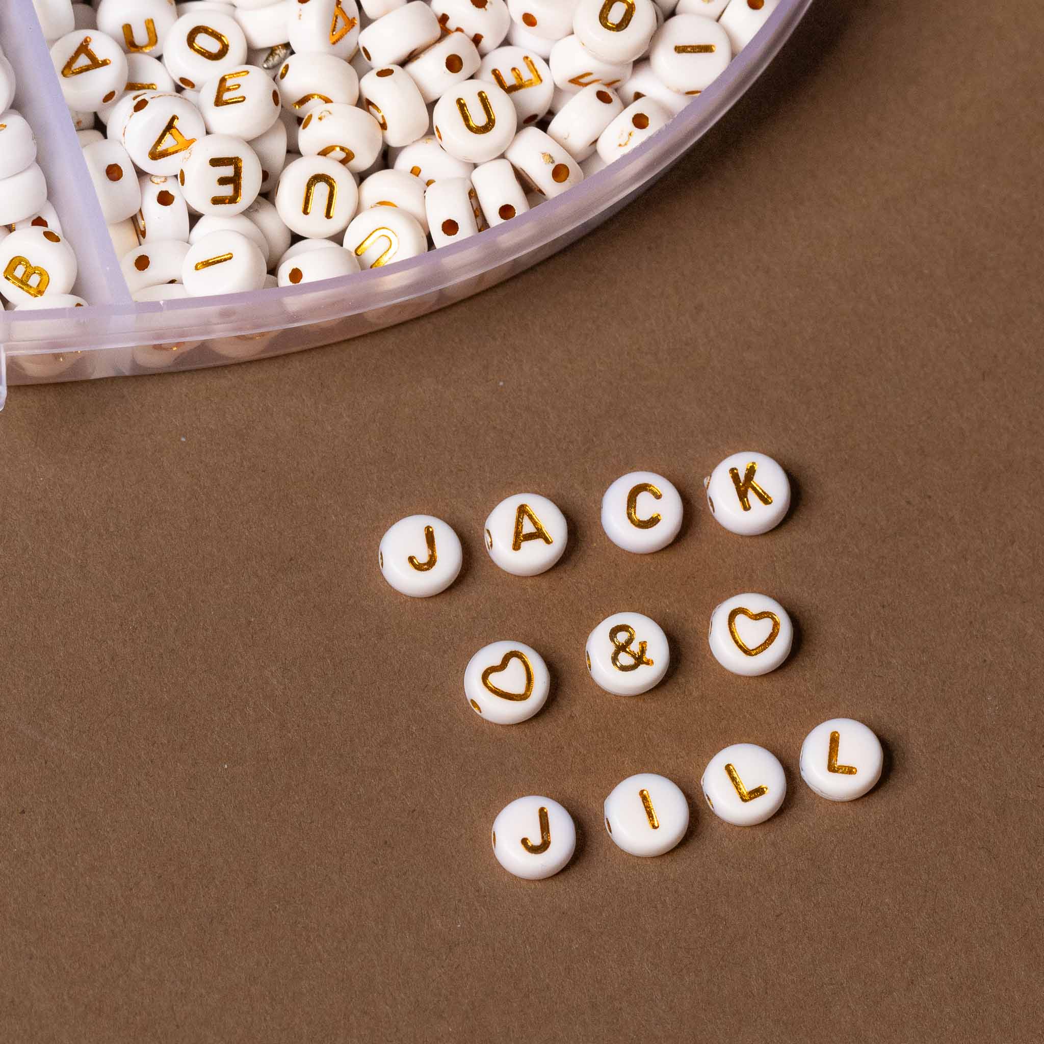 White beads with gold letters spelling 'JACK & JILL' on a brown surface.
