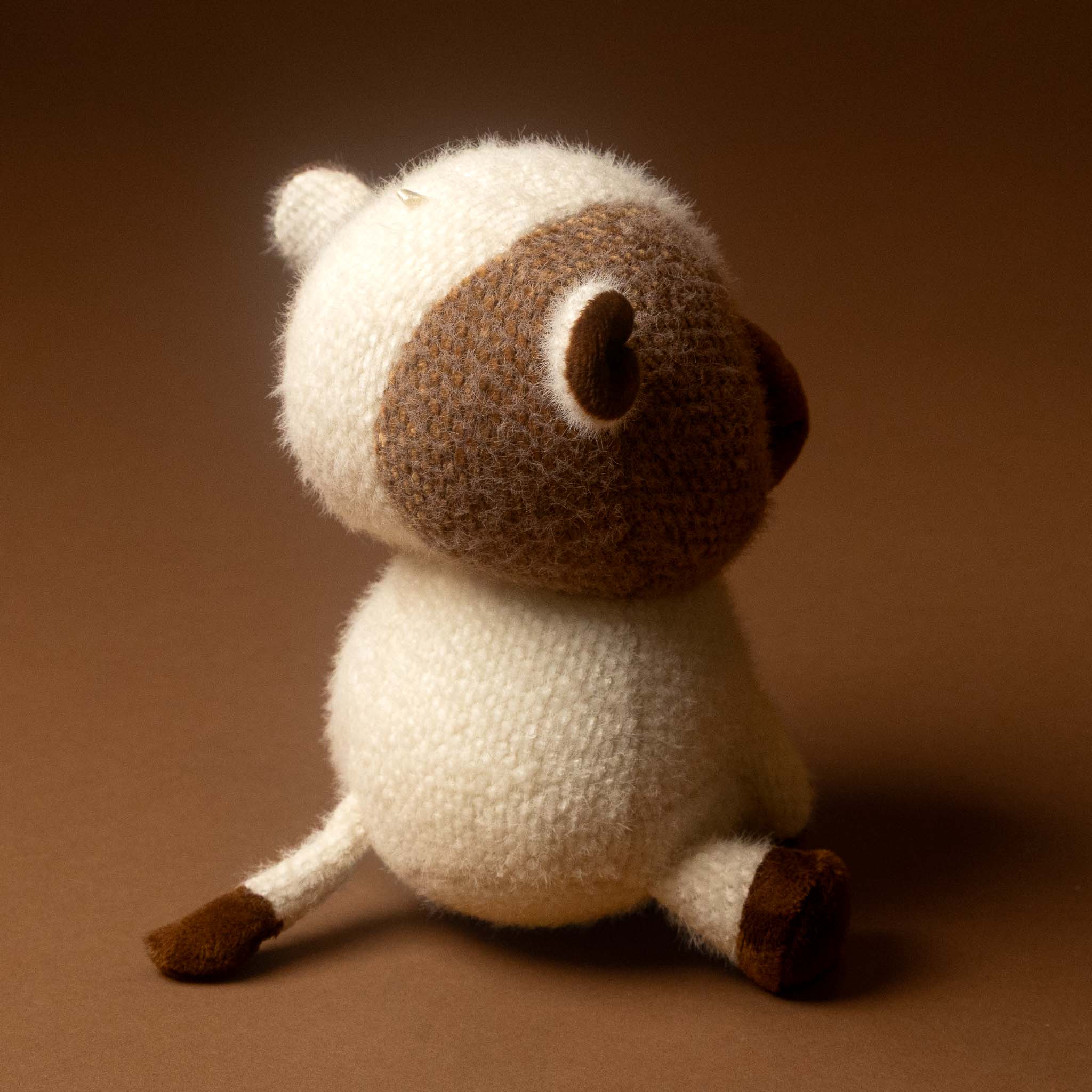 moo-moo-the-cow-small stuffed animal featuring a cream-colored body and head with a brown face patch and dark brown hooves, set against a solid brown background.