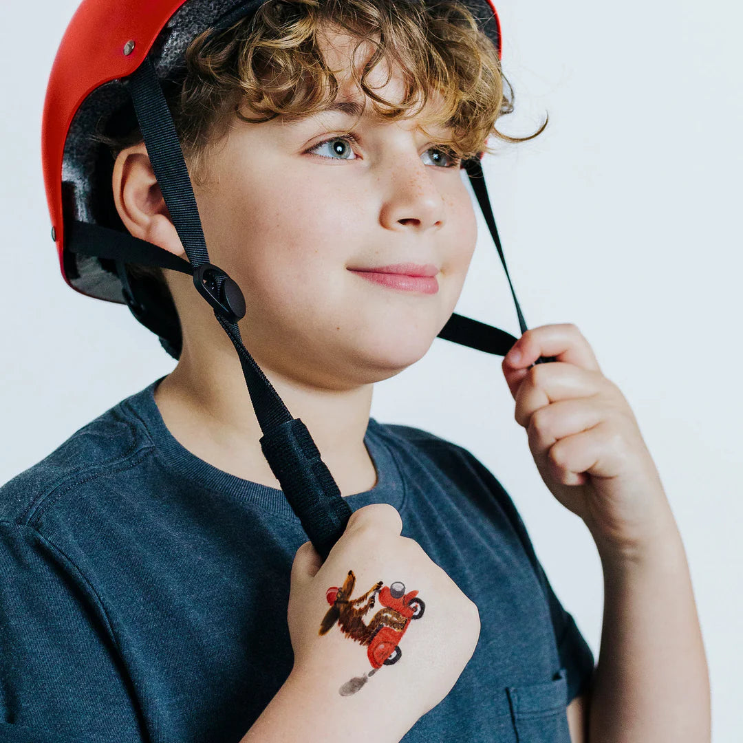 Child wearing a red helmet and moto-pup-temporary-tattoo-pair with a white background