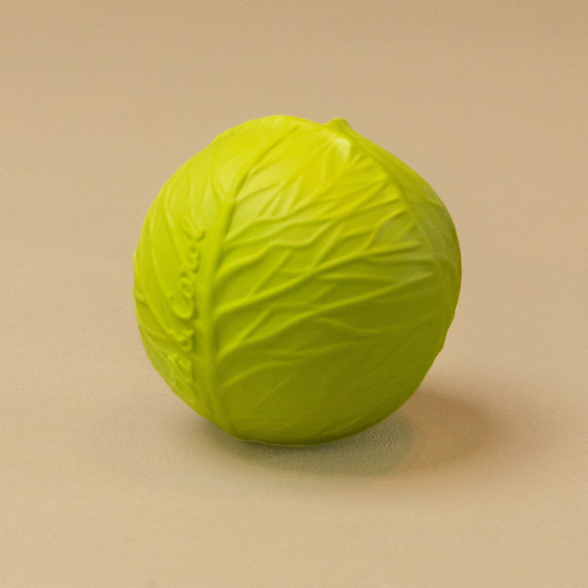 A bright lime green natural-rubber-sensory-ball-cabbage with a textured cabbage leaf pattern, shown on a plain beige background.