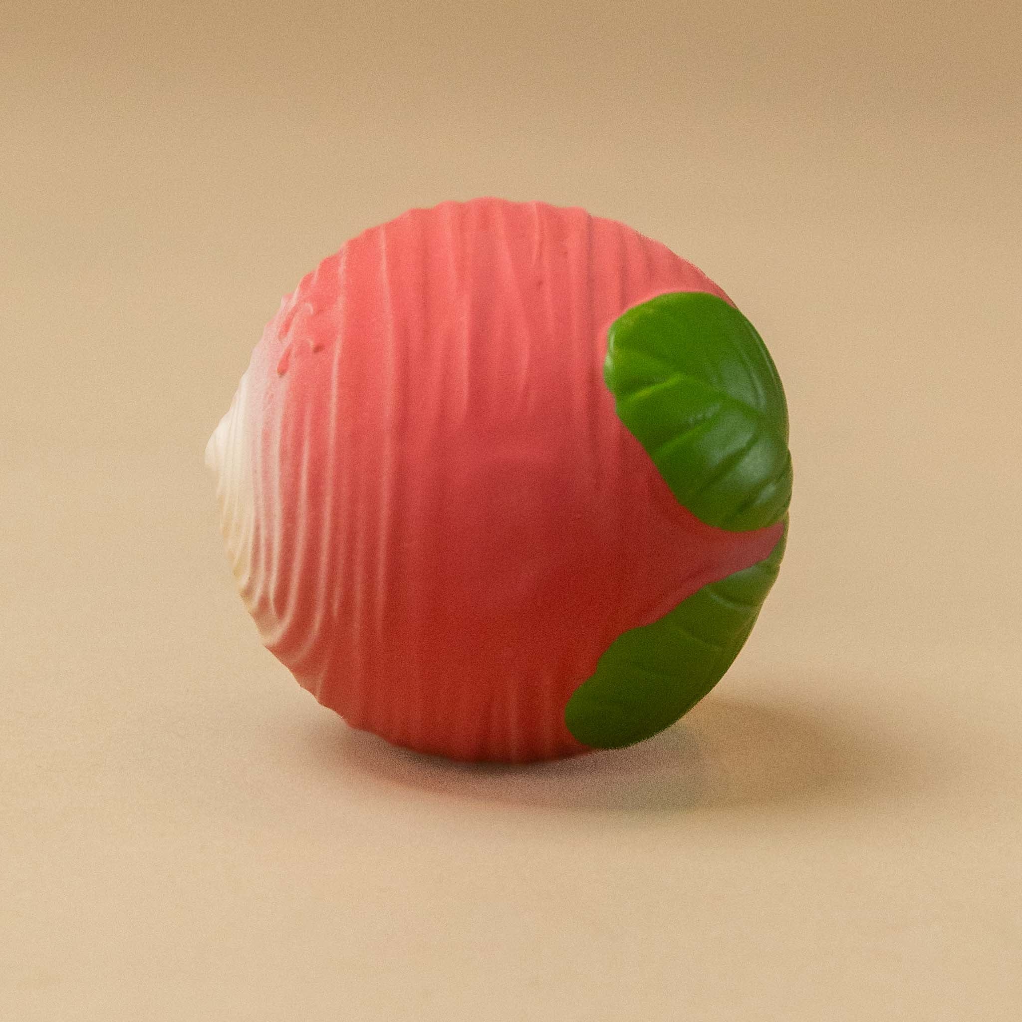 natural-rubber-sensory-ball-radish with a pink-red body, green leaf-like accents, and a white pointed end, photographed on a plain beige background.