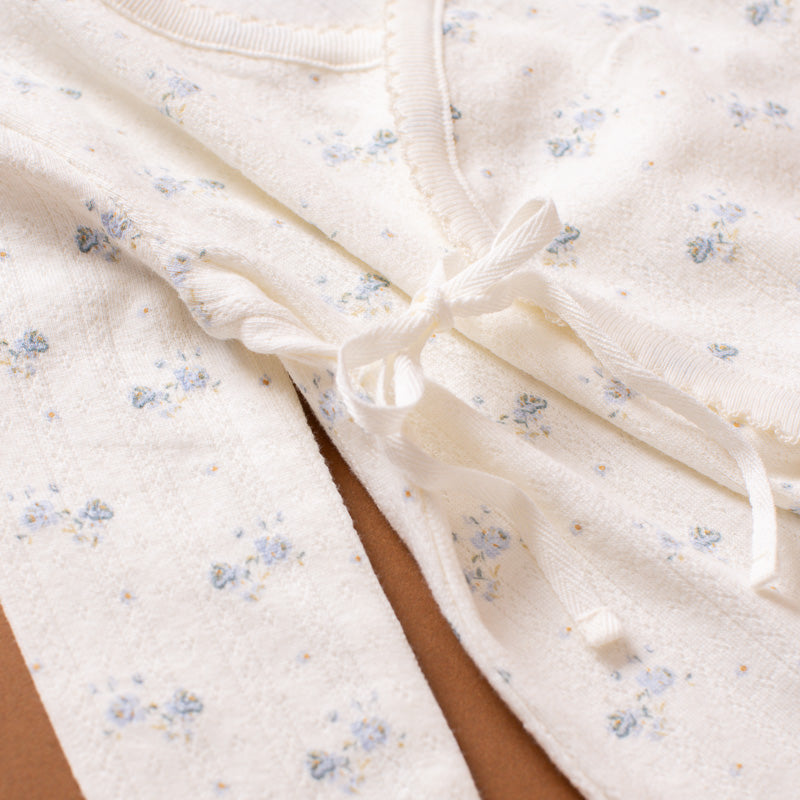 Close-up of a cream-colored cotton garment with a delicate blue and yellow floral print, featuring a matching fabric tie closure.