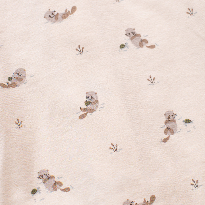 A close-up of a light cream fabric with a repeating pattern of small brown cartoon beavers and tiny tufts of dried grass.