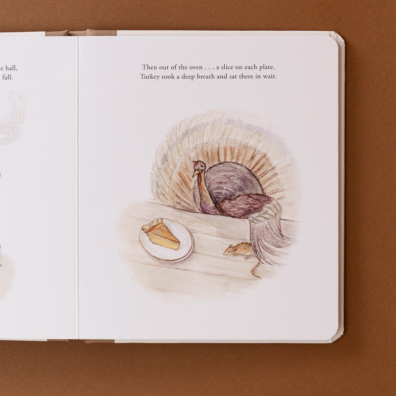 An open children's book spread showing a watercolor-style illustration of a turkey sitting at a table with a slice of pie on a plate, photographed against a brown background.