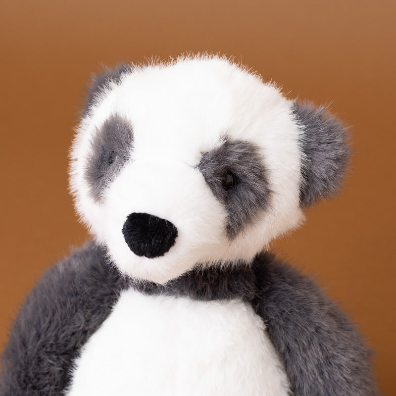 A plush panda toy with black and white fur, a black nose, and dark gray ears, shown against a solid warm brown background.