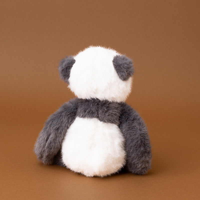 A plush panda toy shown from the back, featuring soft white and dark gray fur, set against a solid warm brown studio background.