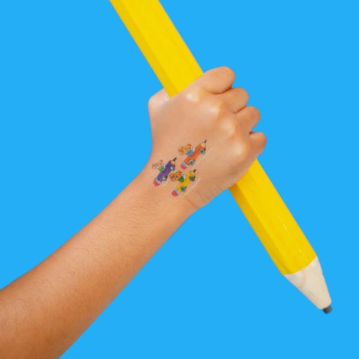 Hand holding a yellow pencil with colorful pencil-cars-temporary-tattoo-pair on a blue background
