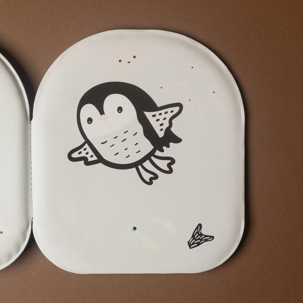 A white penguin--friends-bath-book featuring a black cartoon penguin illustration, shown on a brown background next to another pad.