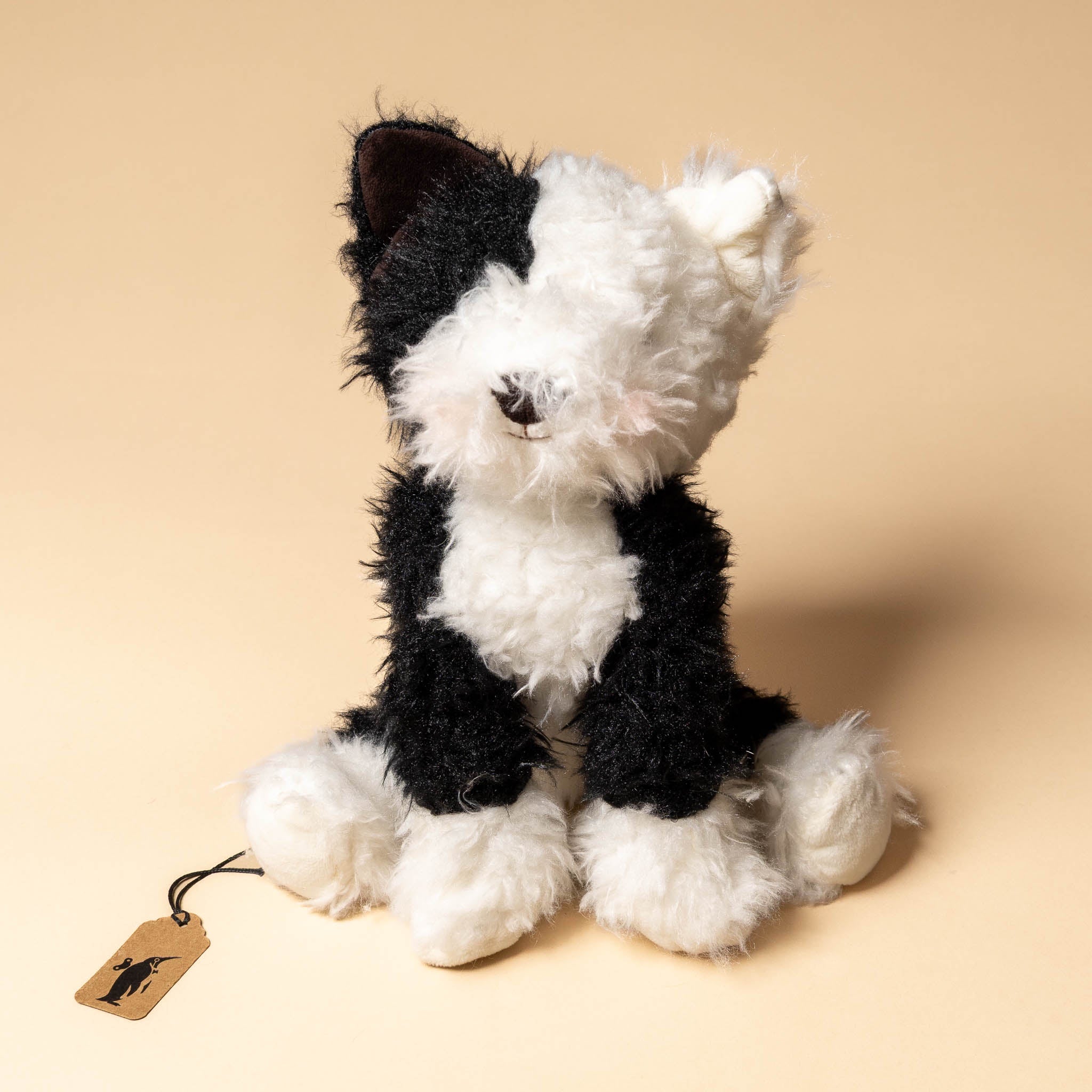 pepper-the-farm-dog Black and white stuffed dog toy with a tag on a beige background