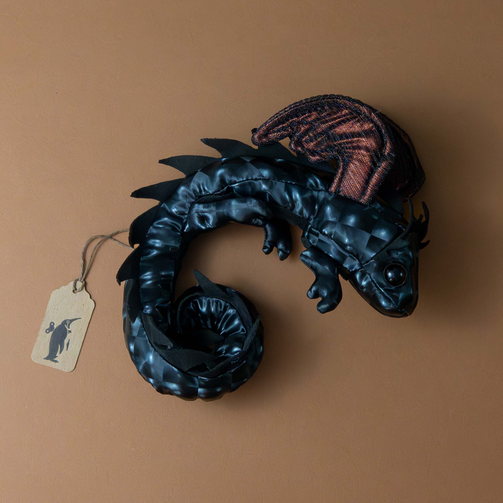 petite-dragon-wristlet-midnight Black dragon figurine with a brown tag on a beige background