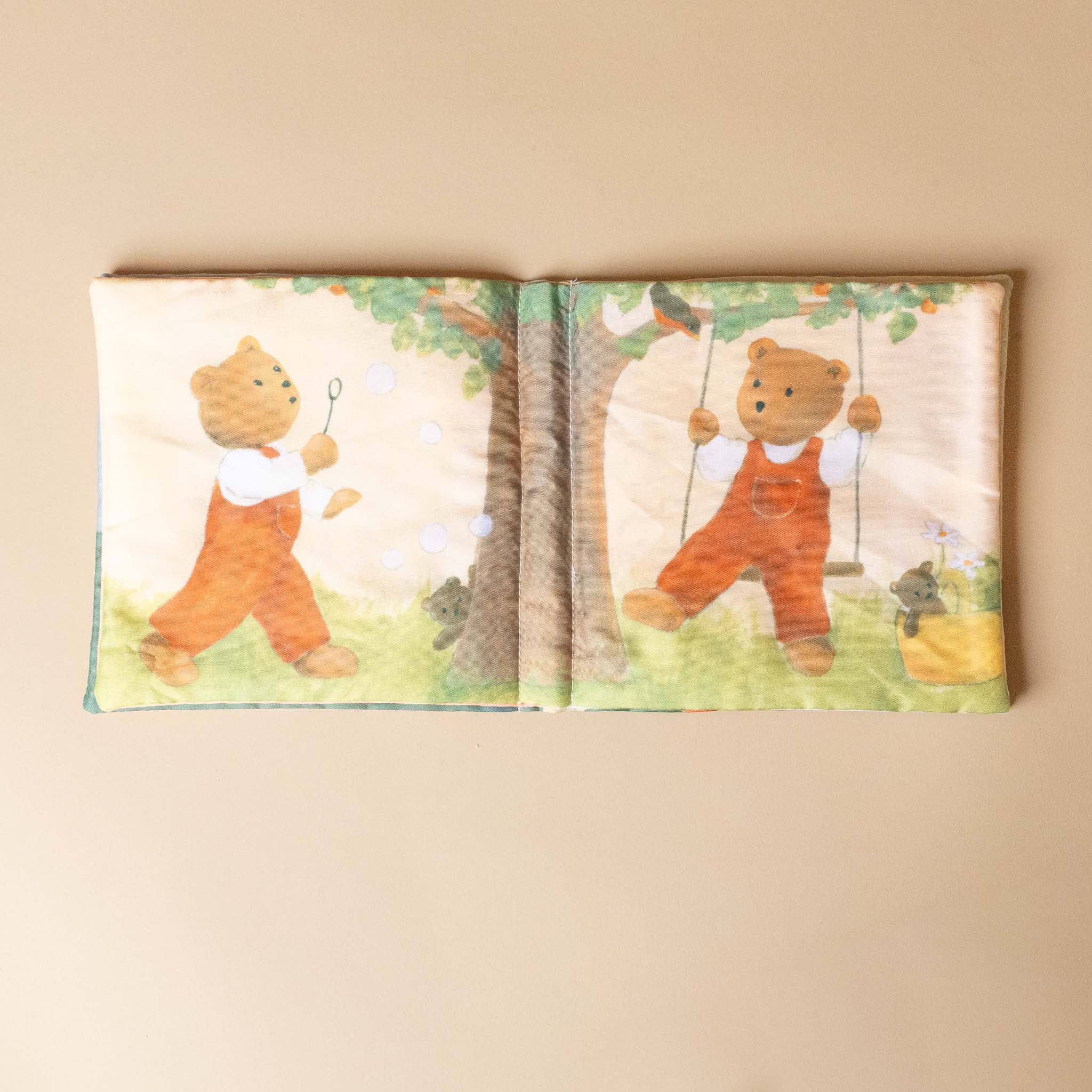 petite-fabric-book-marcel-the-bear Open book with illustrations of a bear in an orange outfit on a beige background