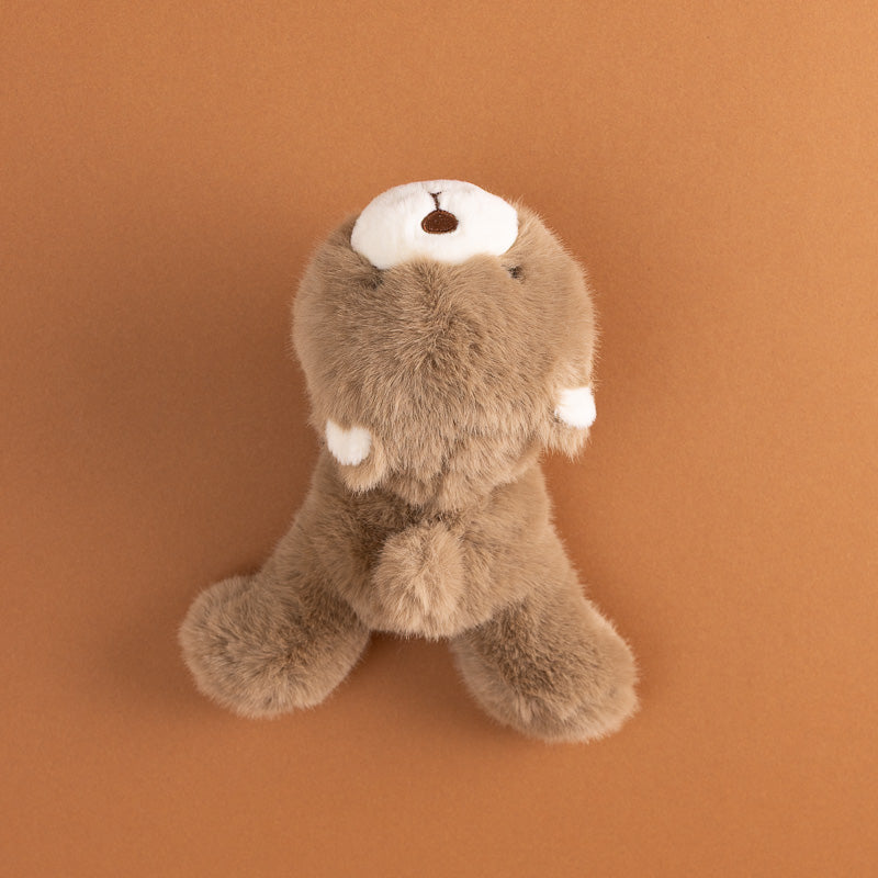 A small plush petite-gluepot-bear in brown faux fur with a white snout and ears, sitting on a solid warm brown background