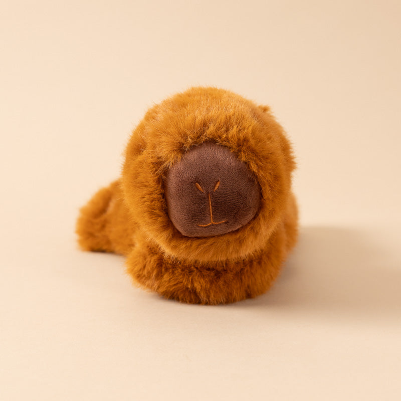 A small brown plush petite-gluepot-capybara toy lying on its side on a warm cream background