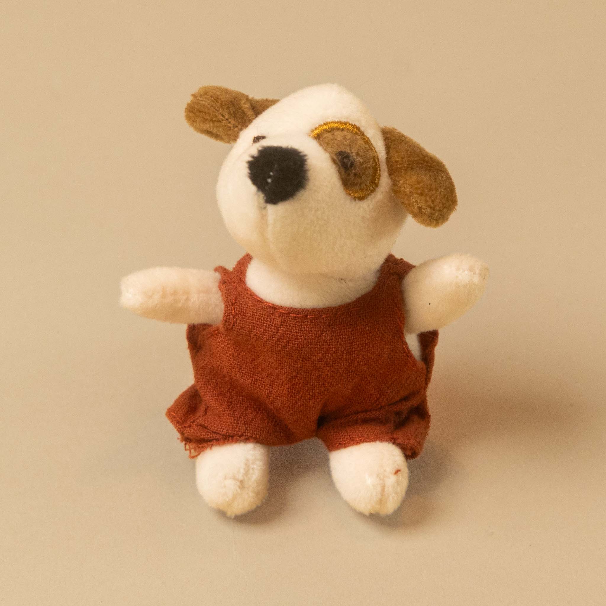 A small plush dog toy with white and brown fur, wearing a rust-red overall petits-amis-eddie-pup