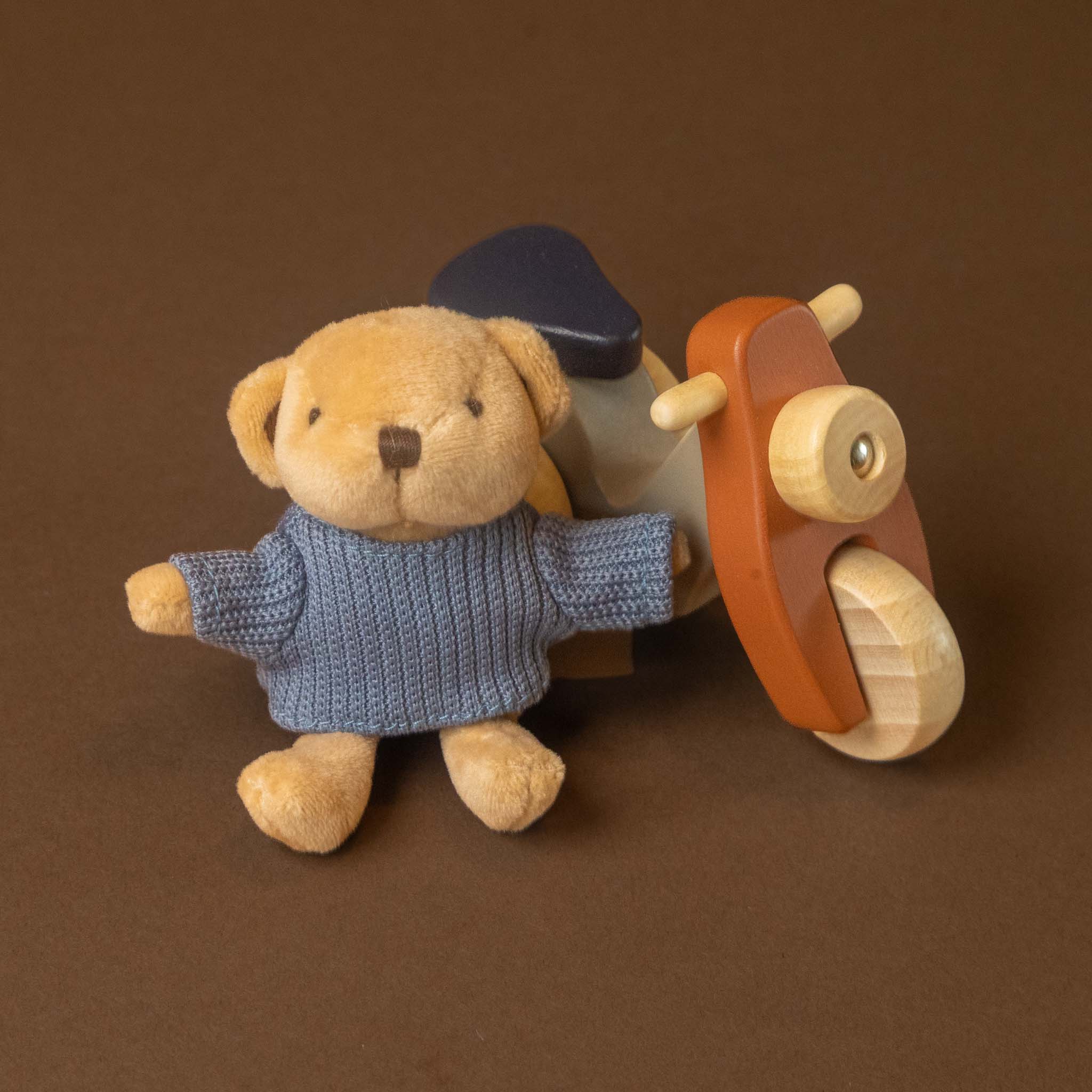 petits-amis-scooter-alexis-bear toy wearing a blue knit sweater, posed next to a wooden toy moped on a solid brown background.