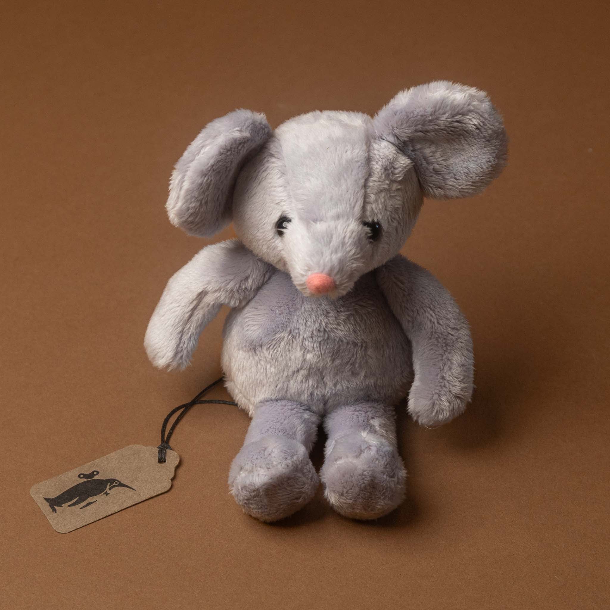 Gray plush pip-the-mouse toy with a tag on a brown background