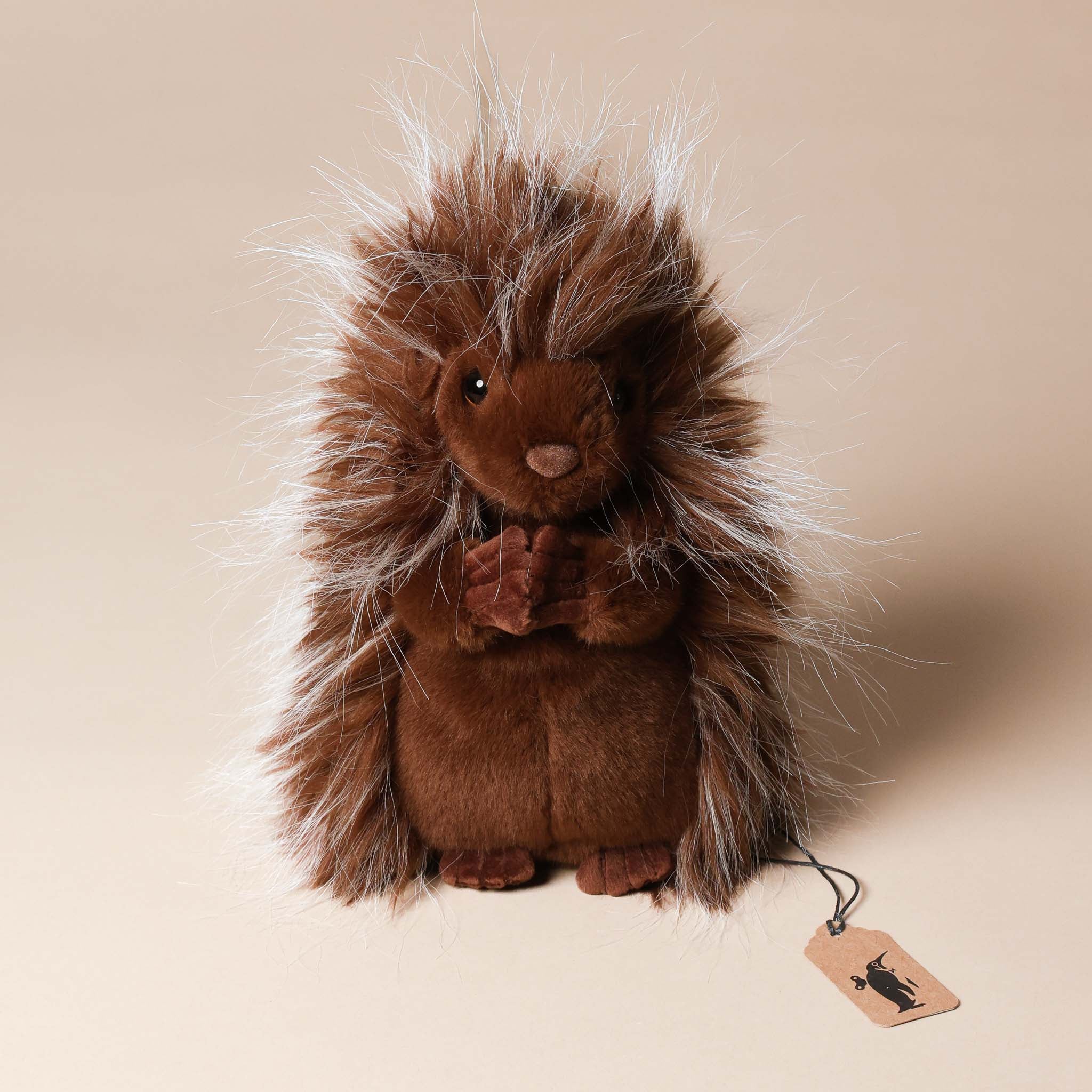 Plush toy prickle-the-porcupine with a tag on a beige background