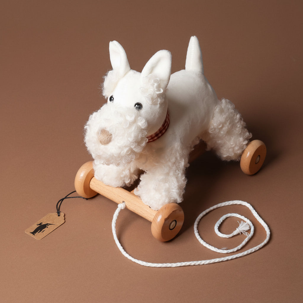White pull-along-lola-the-dog toy with wooden wheels on a brown background