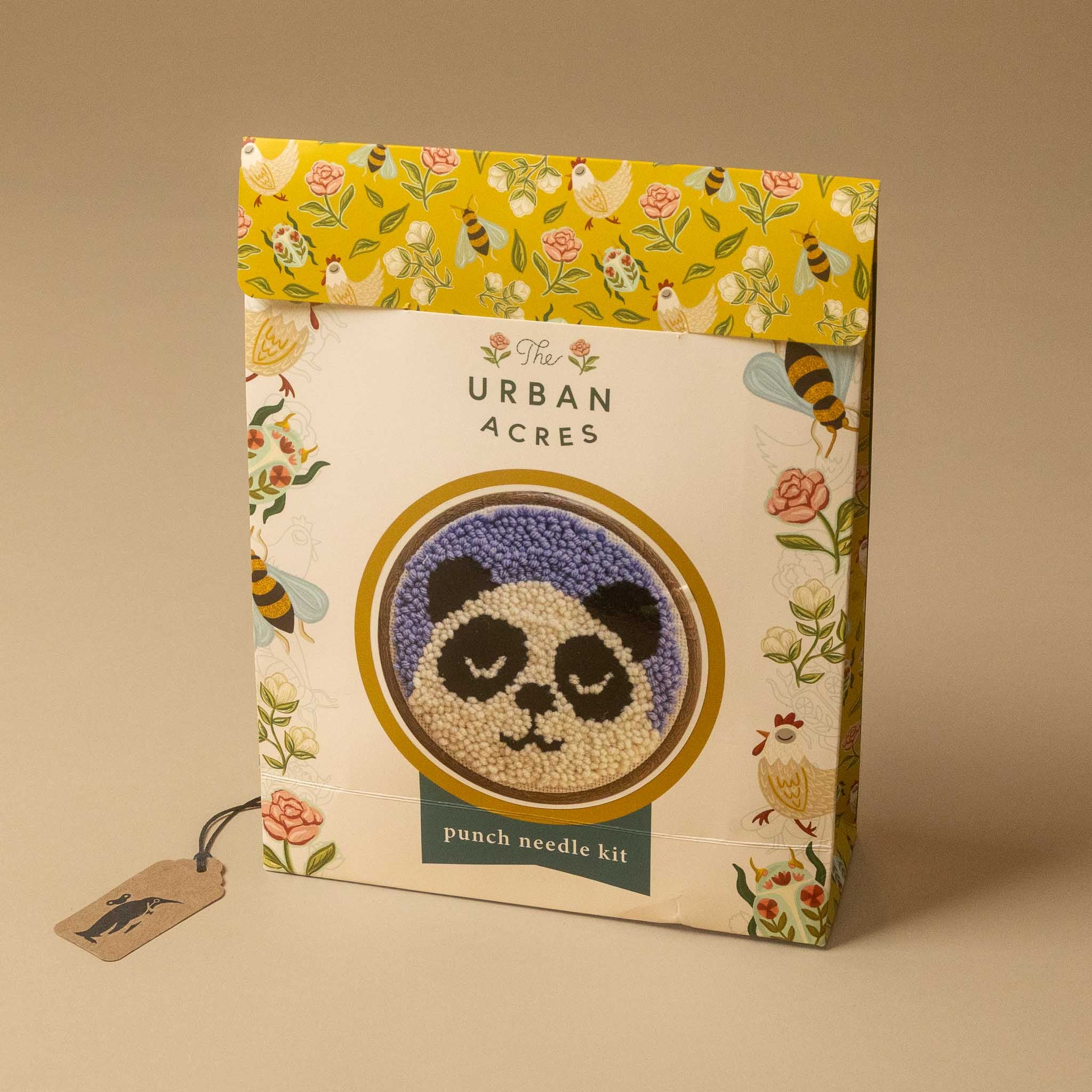 The Punch Needle Kit box featuring a panda design, with a yellow floral patterned top flap and a hanging paper tag, set against a solid beige background.