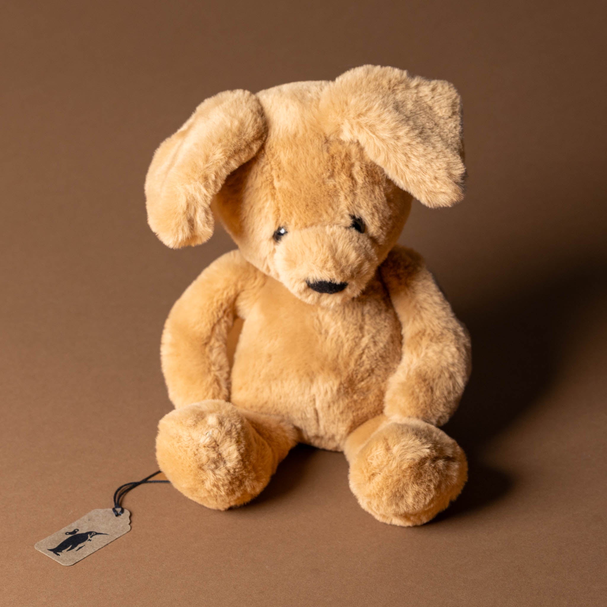 ruff-the-pup-oatmeal Beige stuffed dog toy with a tag on a brown background