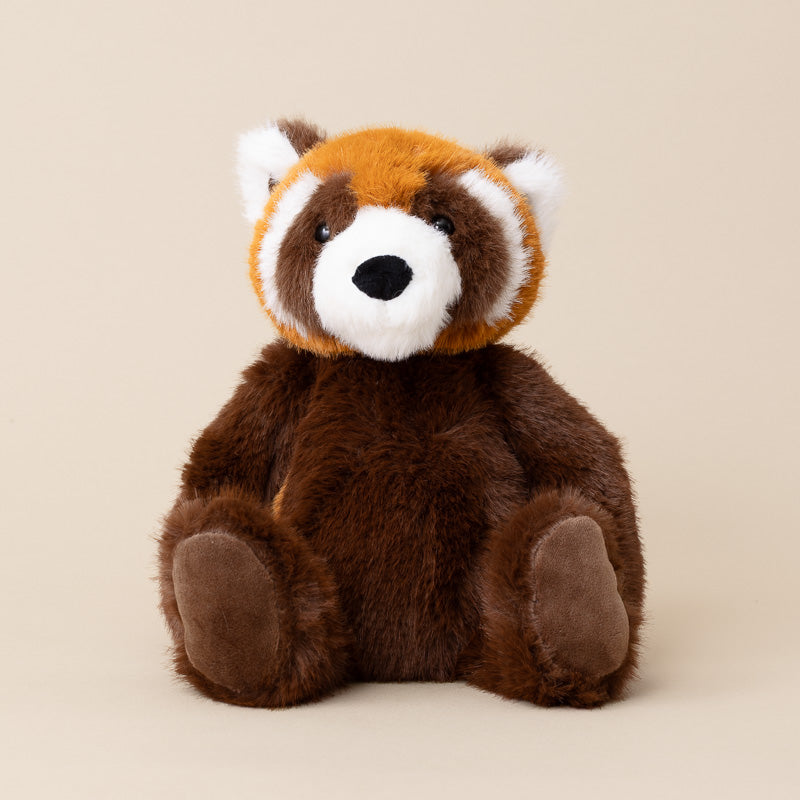 A plush red panda stuffed animal sitting upright against a solid beige background. The toy features brown fur on its body, orange fur on its head, and white markings around its face and ears.