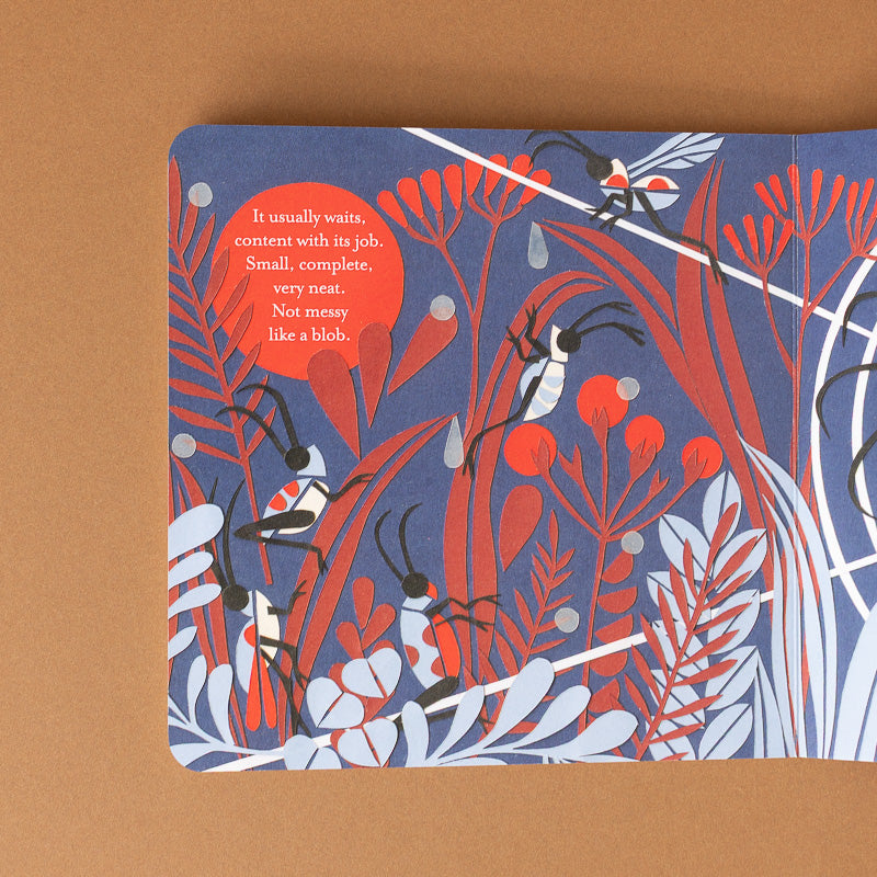 A square printed card or book page featuring an illustrated botanical and insect design in coral red, white, and dark blue, placed on a tan background. A red circular text bubble appears on the left side.