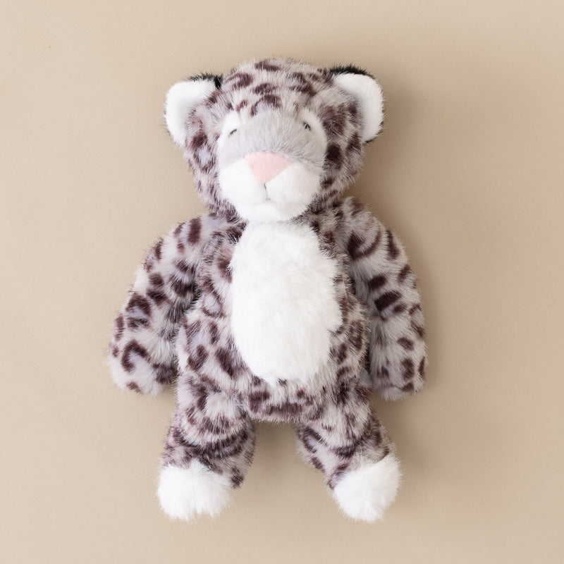 A plush stuffed animal toy shaped like a spotted big cat, featuring a faux fur texture in gray, white, and dark brown, with a pink nose, set against a solid beige background.