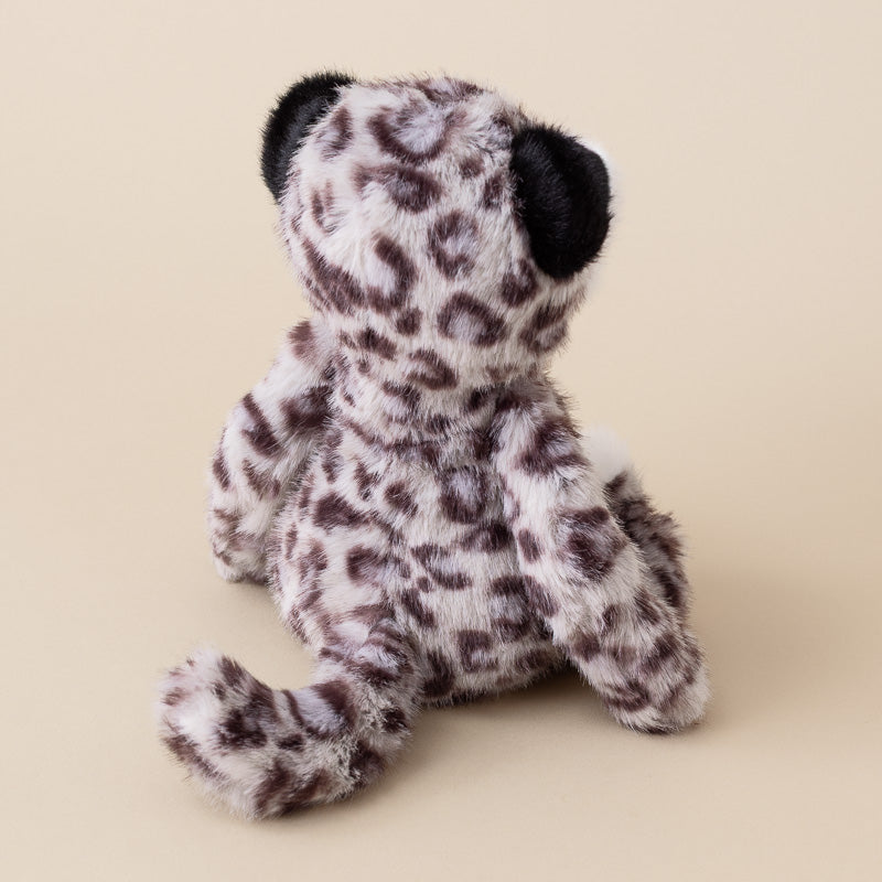A plush leopard toy shown from the back, featuring a white and dark brown spotted fur pattern with black ears, set against a solid beige background.
