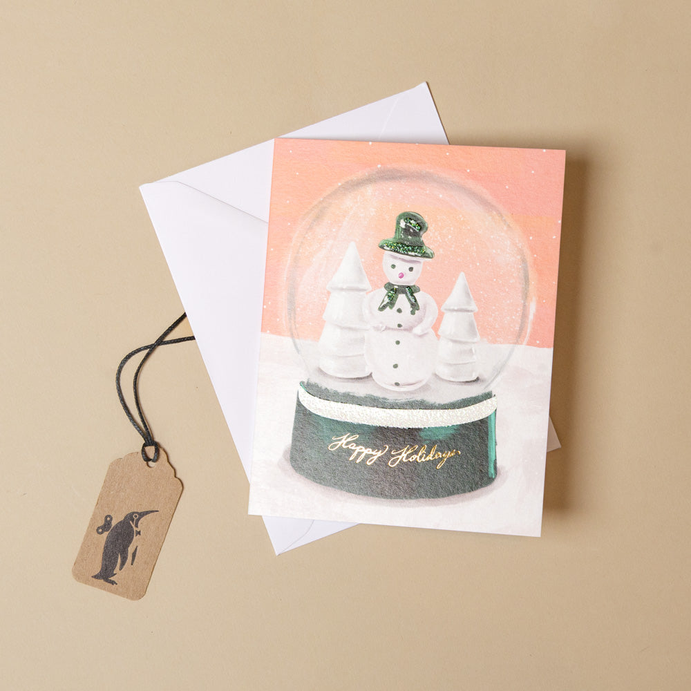 snowglobe-holidays-greeting-card with a snow globe design featuring a snowman and trees, on a brown background.
