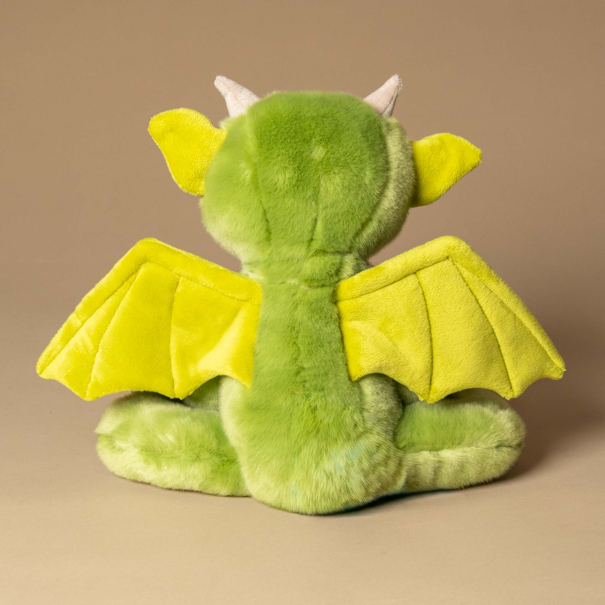 spires-the-forest-gargoyle Green plush dragon toy with yellow wings on a beige background