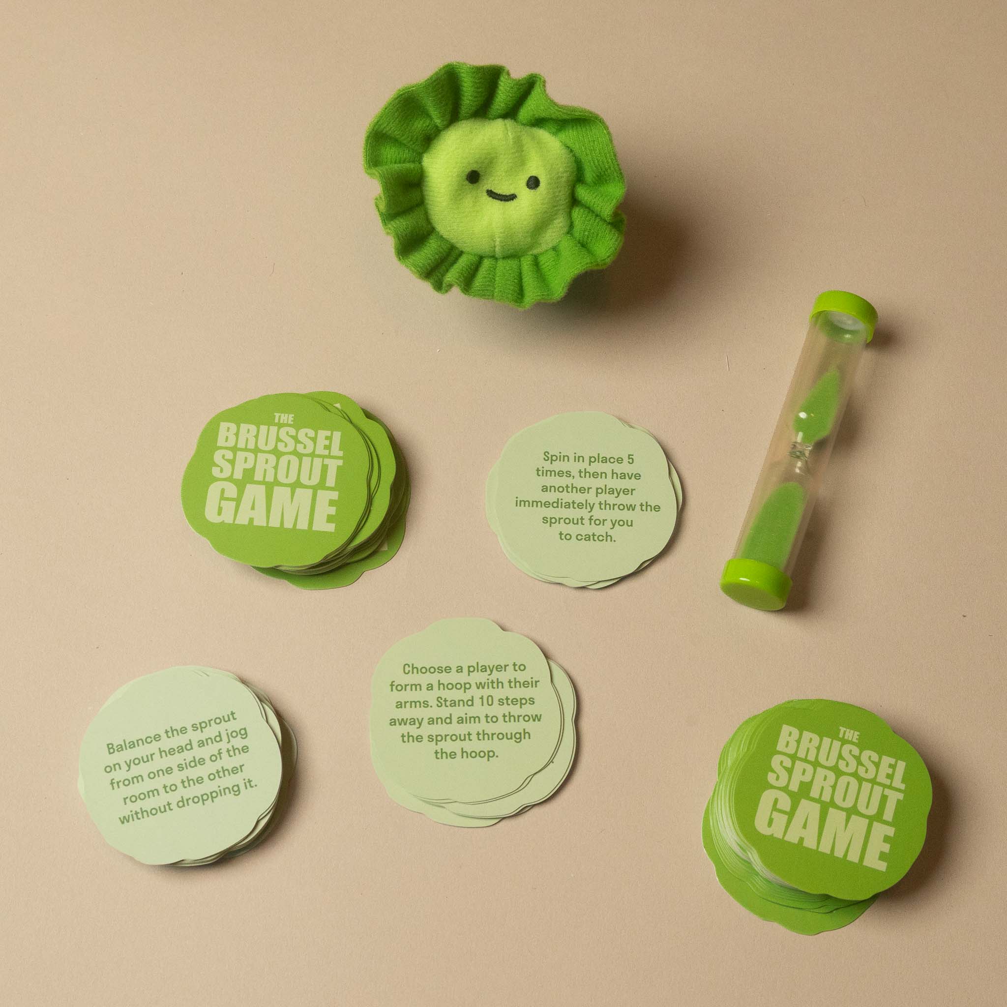 Brussel Sprout Game set on a beige background, including a green plush sprout, a clear tube with a green cap, and multiple round game tokens and instruction cards.