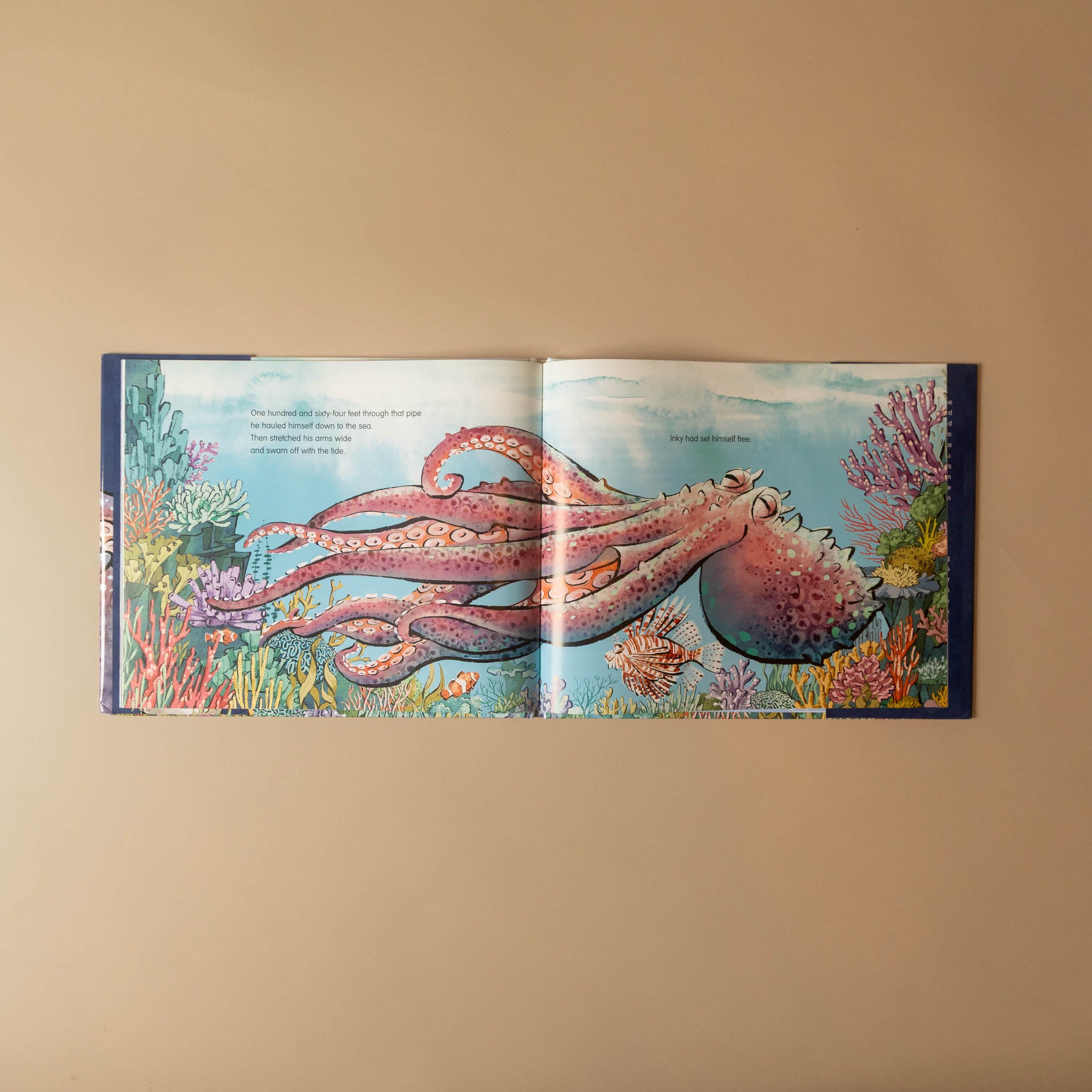 An open children's picture book showing a colorful underwater illustration of a pink octopus with coral reef and fish, displayed against a plain beige background.