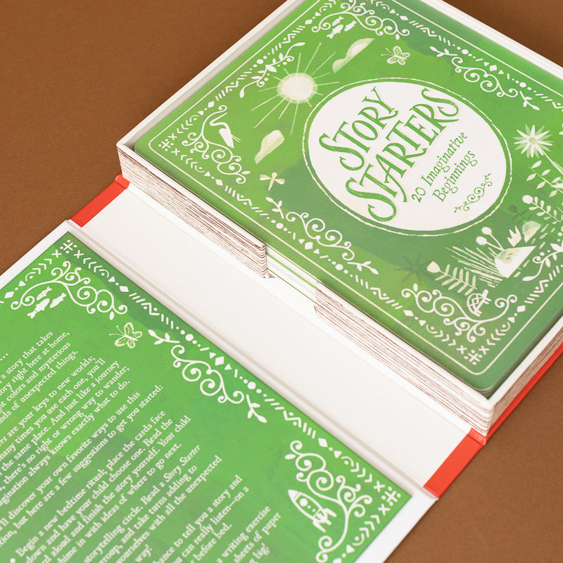 A deck of 'Story Starters' cards shown open on a brown background, featuring a green and white illustrated cover with text prompts inside.