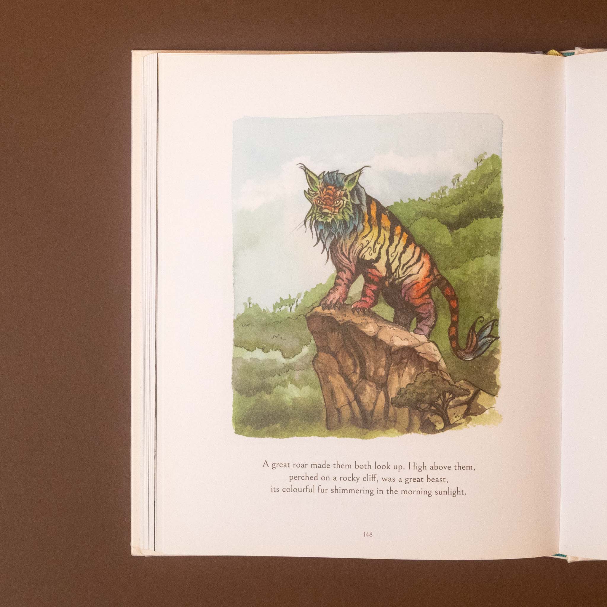 An open book spread showing a vintage-style illustrated page with a colorful tiger standing on a rock in a landscape, accompanied by a short poem. The book pages are photographed against a dark brown background.