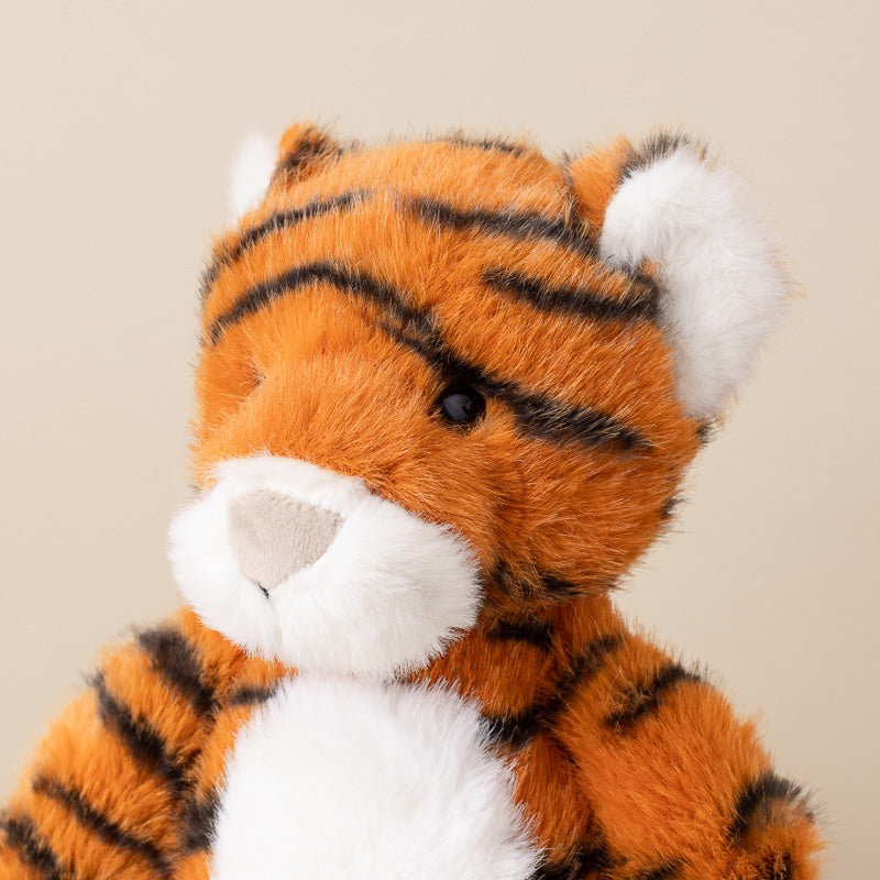 A close-up of a plush tiger toy with orange fur, black stripes, and white accents on its face, ears, and chest, set against a plain beige background.