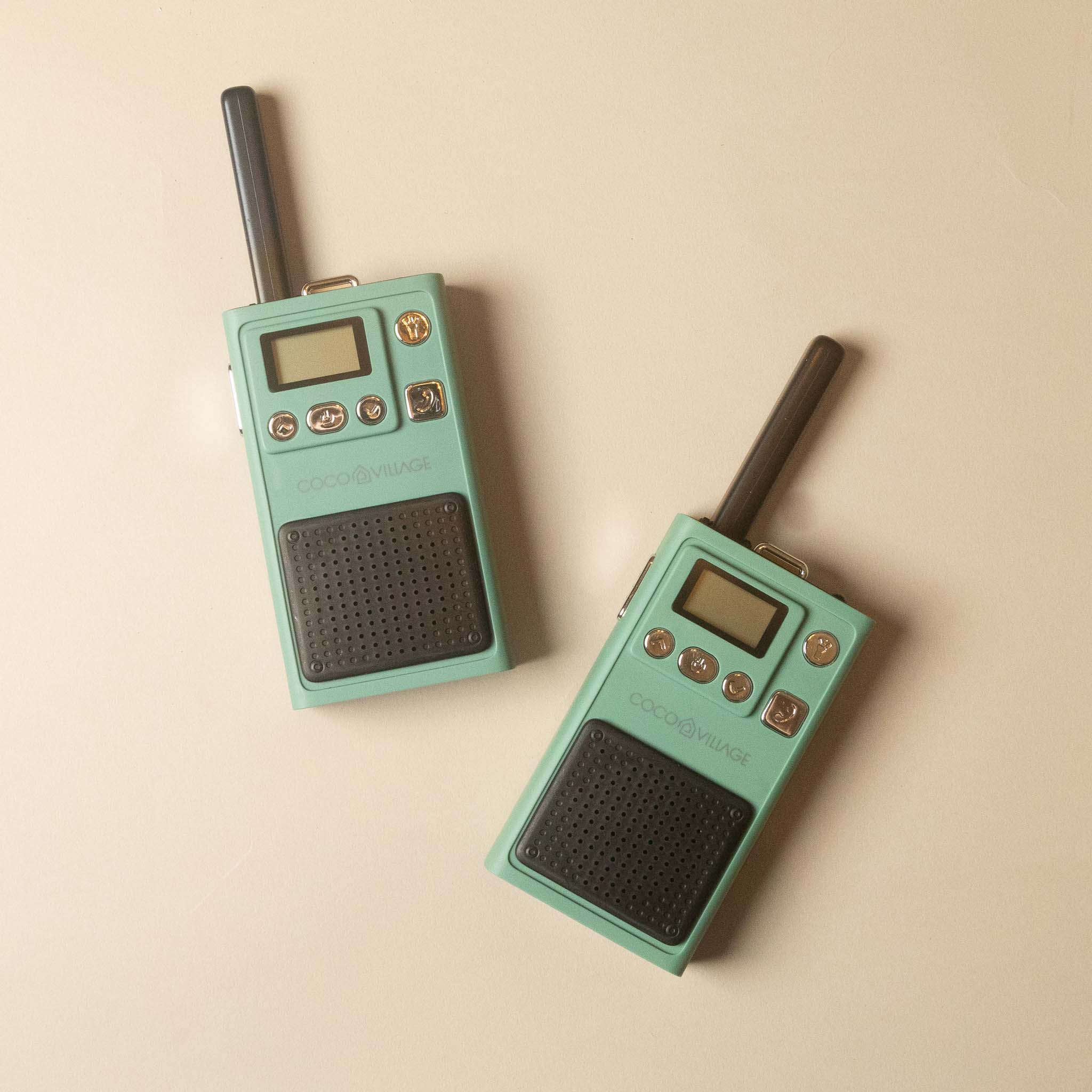 Two vintage-style walkie-talkies in mint green with black antennas and speaker grilles, arranged diagonally on a warm beige background.