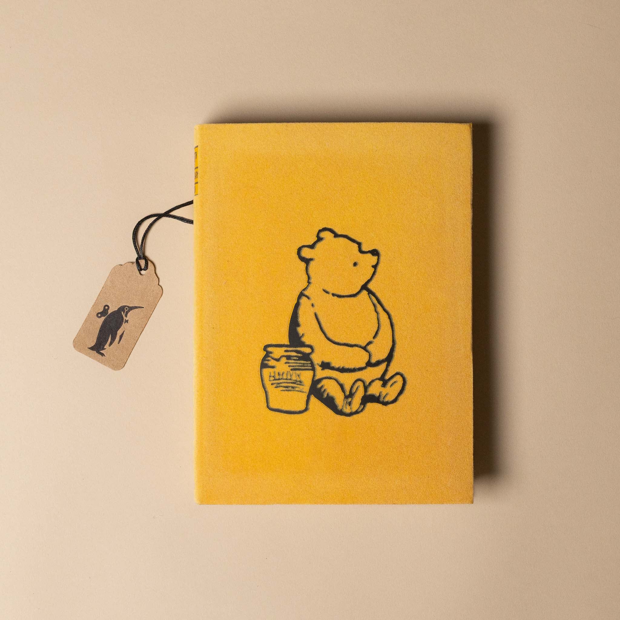 Yellow winnie-the-pooh-100th-anniversary-edition with a bear illustration and honey jar, featuring a tag on a beige background