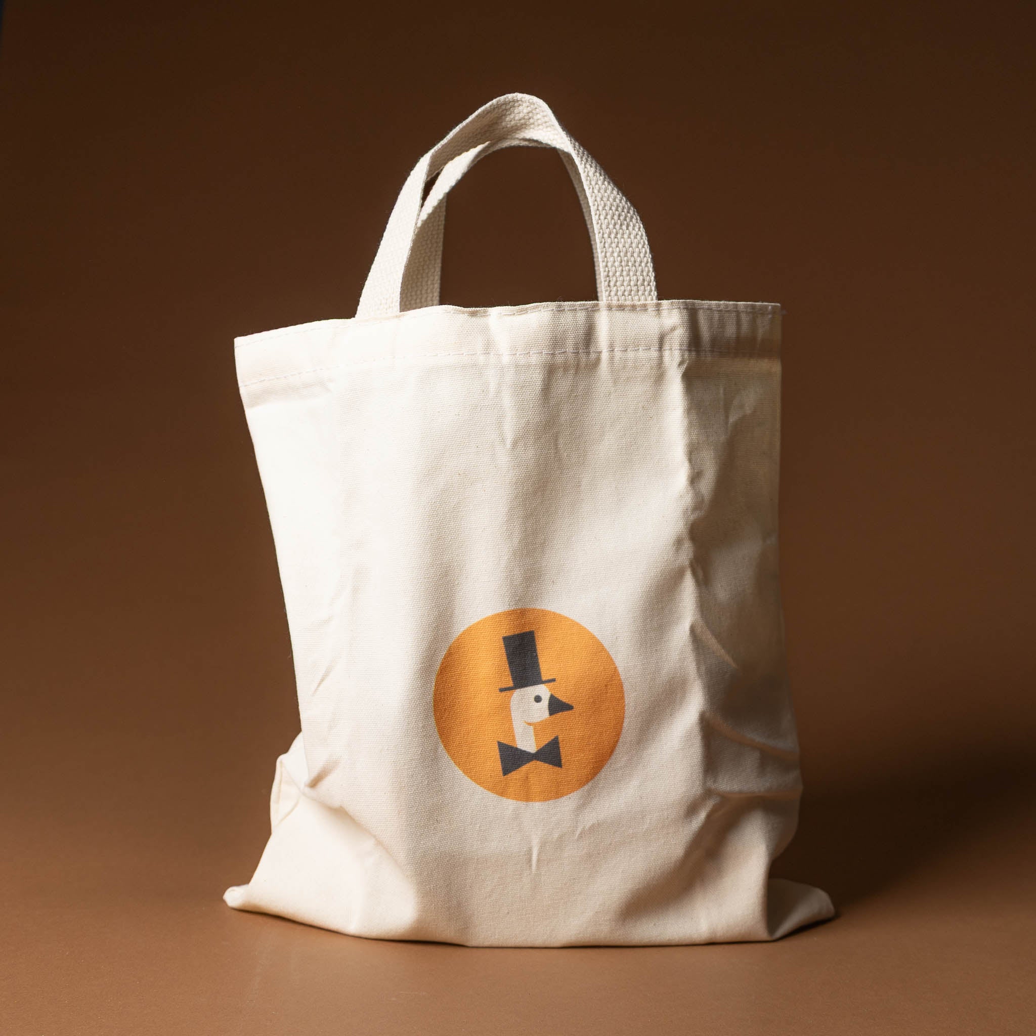 wooden-block-set-with-canvas-bag-classic-abcs Beige tote bag with a circular logo featuring a top hat and bow tie on a brown background