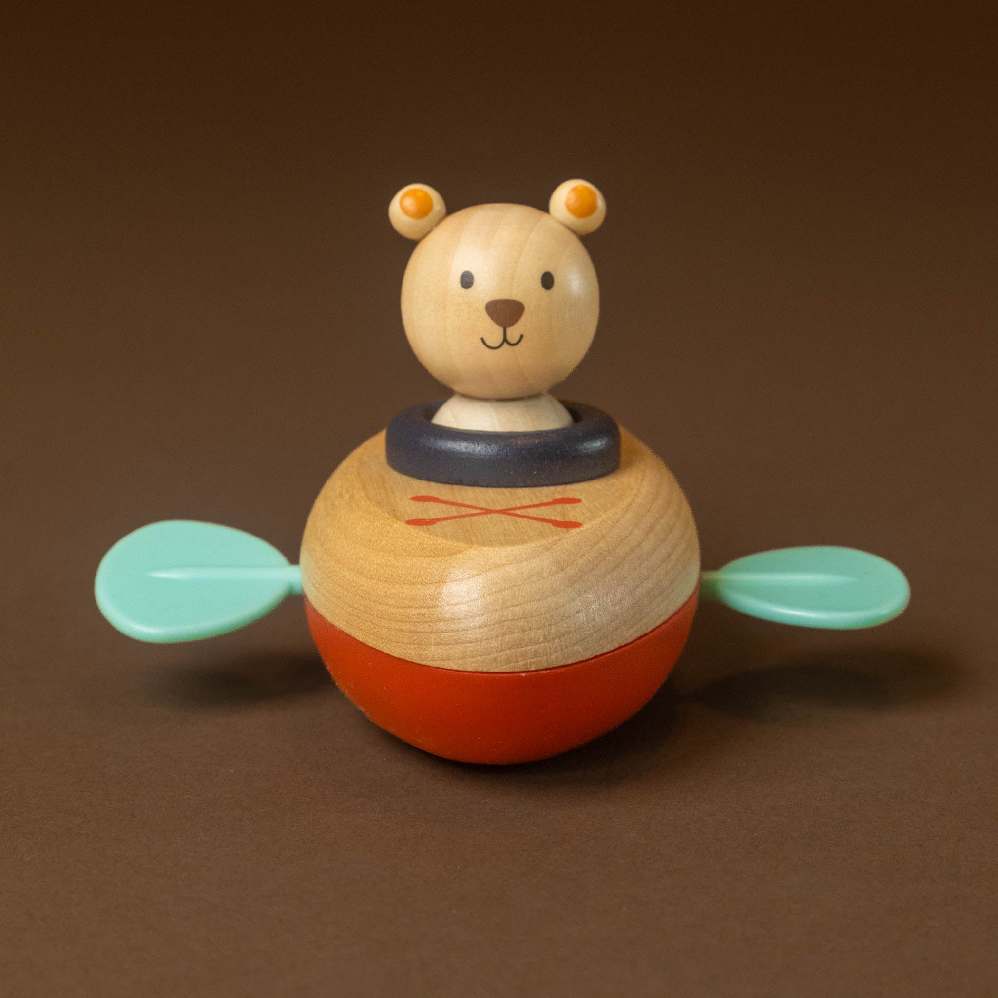 wooden-clockwork-float-boat-bear with a natural wood head, a dark blue collar, an orange-red body, and two mint green paddle-like arms, photographed on a plain brown background.