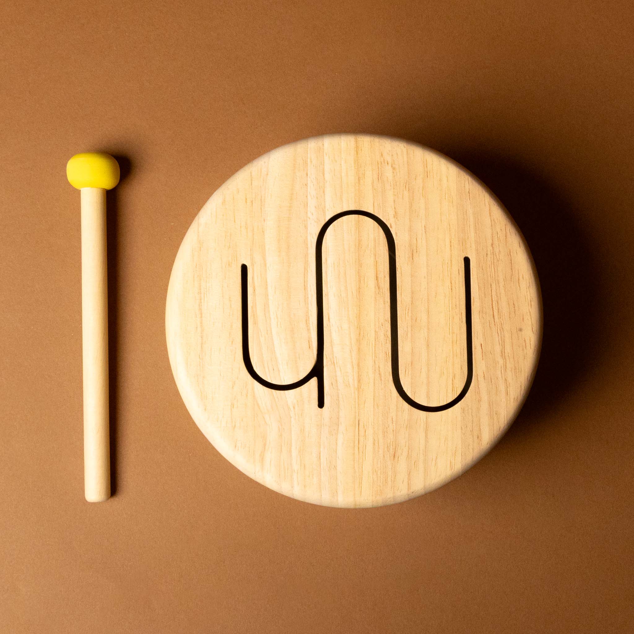 Wooden toy drum with colorful patterns and a drumstick on a brown background