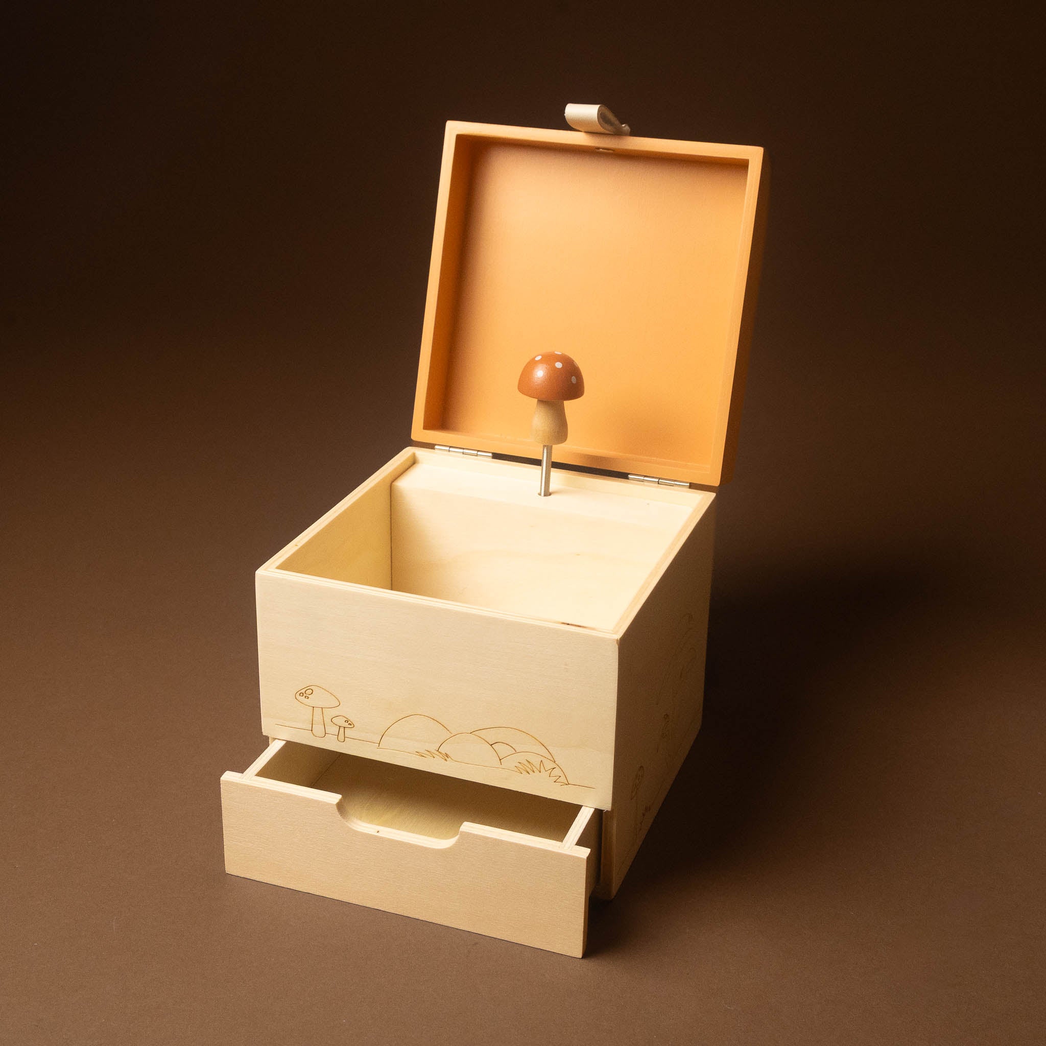 wooden-musical-treasures-box-nature with an open lid and a partially pulled-out drawer, featuring a miniature mushroom figure on a pin inside. The box is made of light natural wood with a warm peach-toned interior, set against a dark brown background.