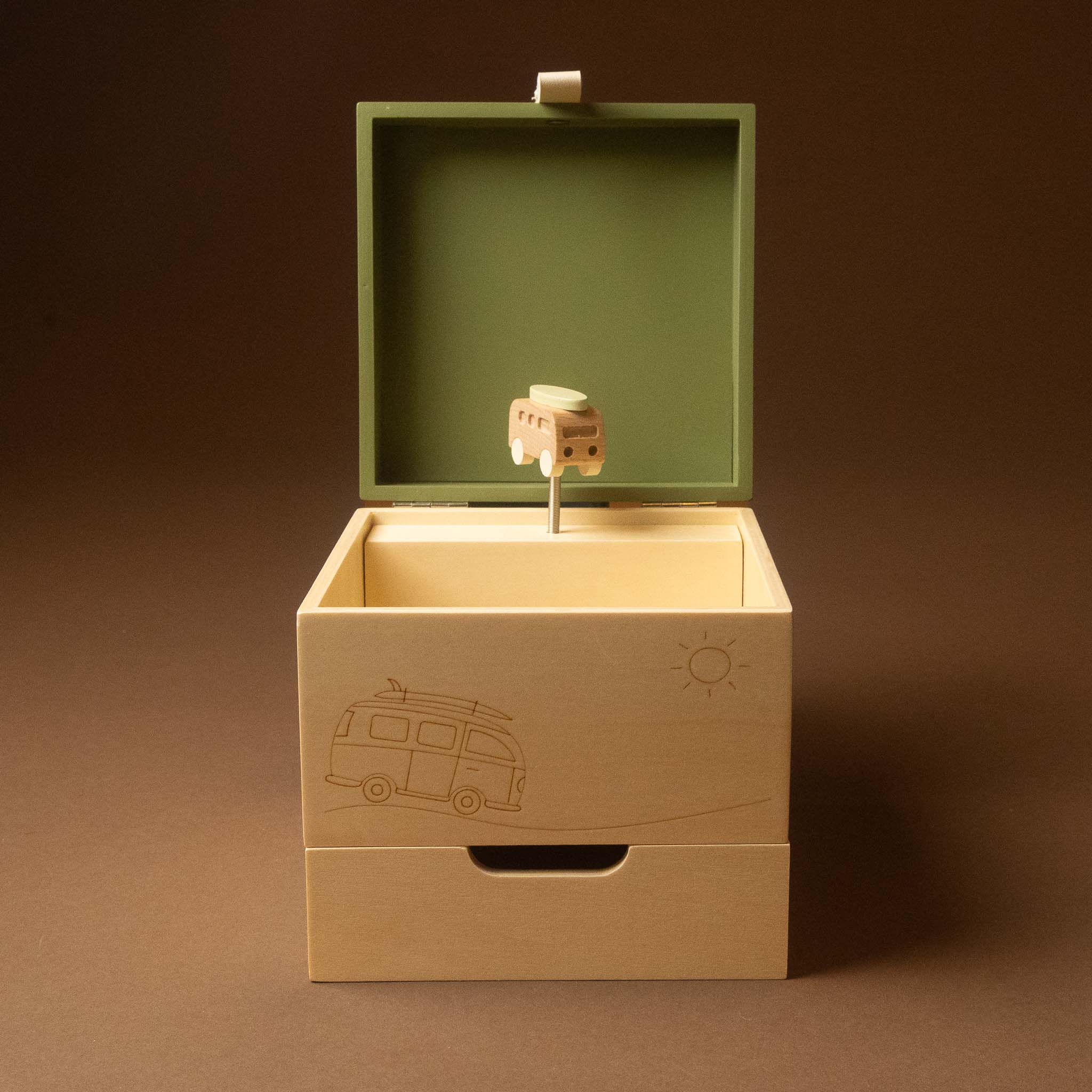 wooden-musical-treasures-box-road-warrier with its lid open, featuring a small tree-and-train mechanism inside. The box is light natural wood with engraved illustrations of a van and a sun, and has a muted green interior lid lining, set against a dark brown background.