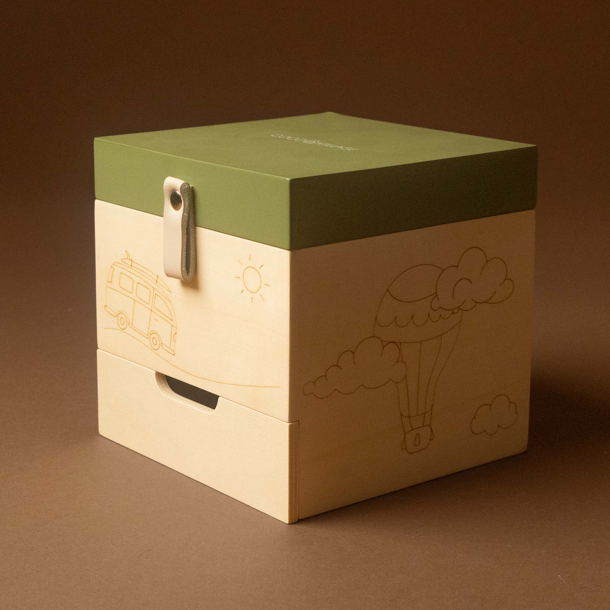 wooden-musical-treasures-box-road-warrier with a green top lid and a light natural wood drawer front, featuring engraved illustrations of a van, sun, hot air balloon, and clouds. The box is photographed on a solid brown background.