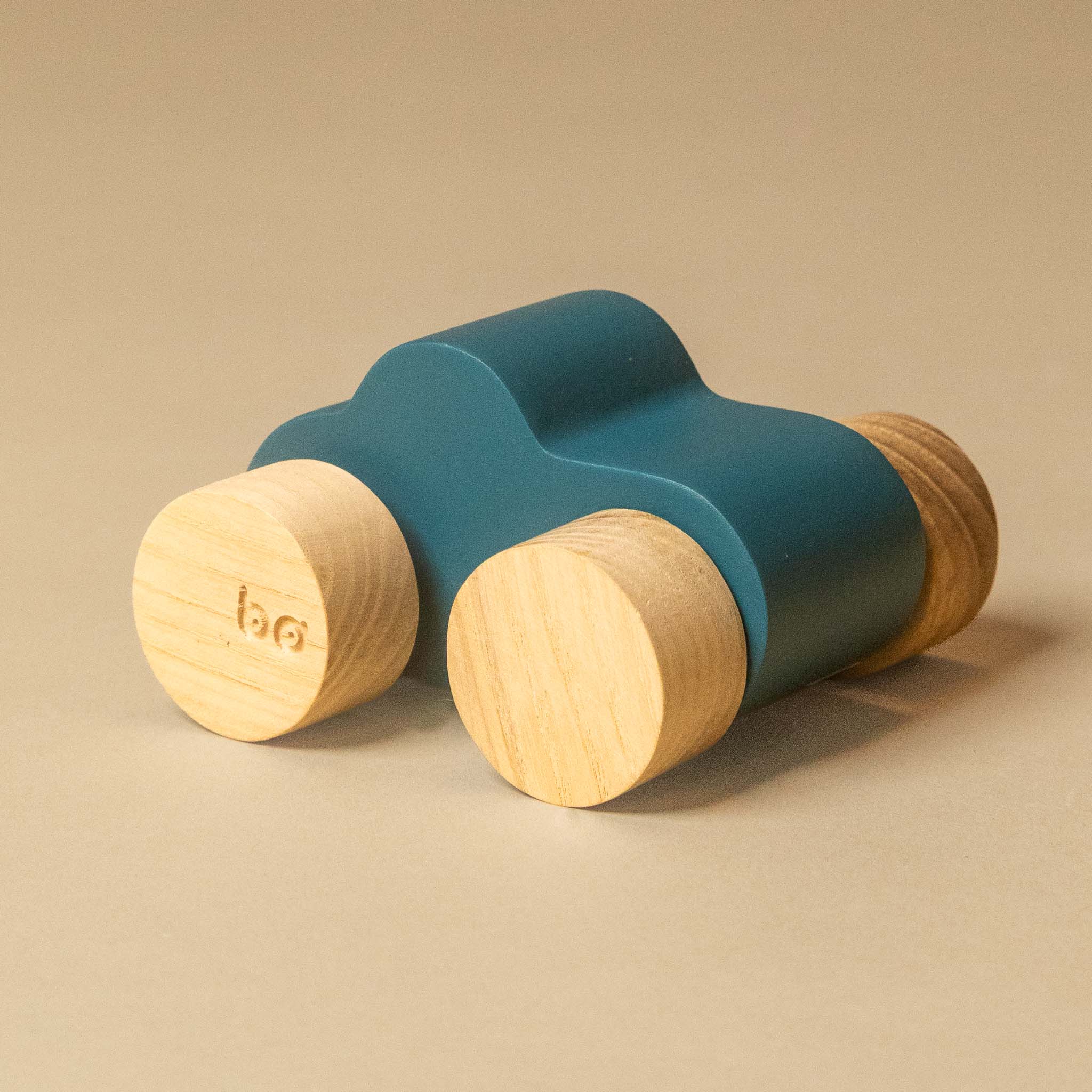 A modern wooden car made of matte blue painted plastic and natural light wood wheels, photographed on a warm beige background.