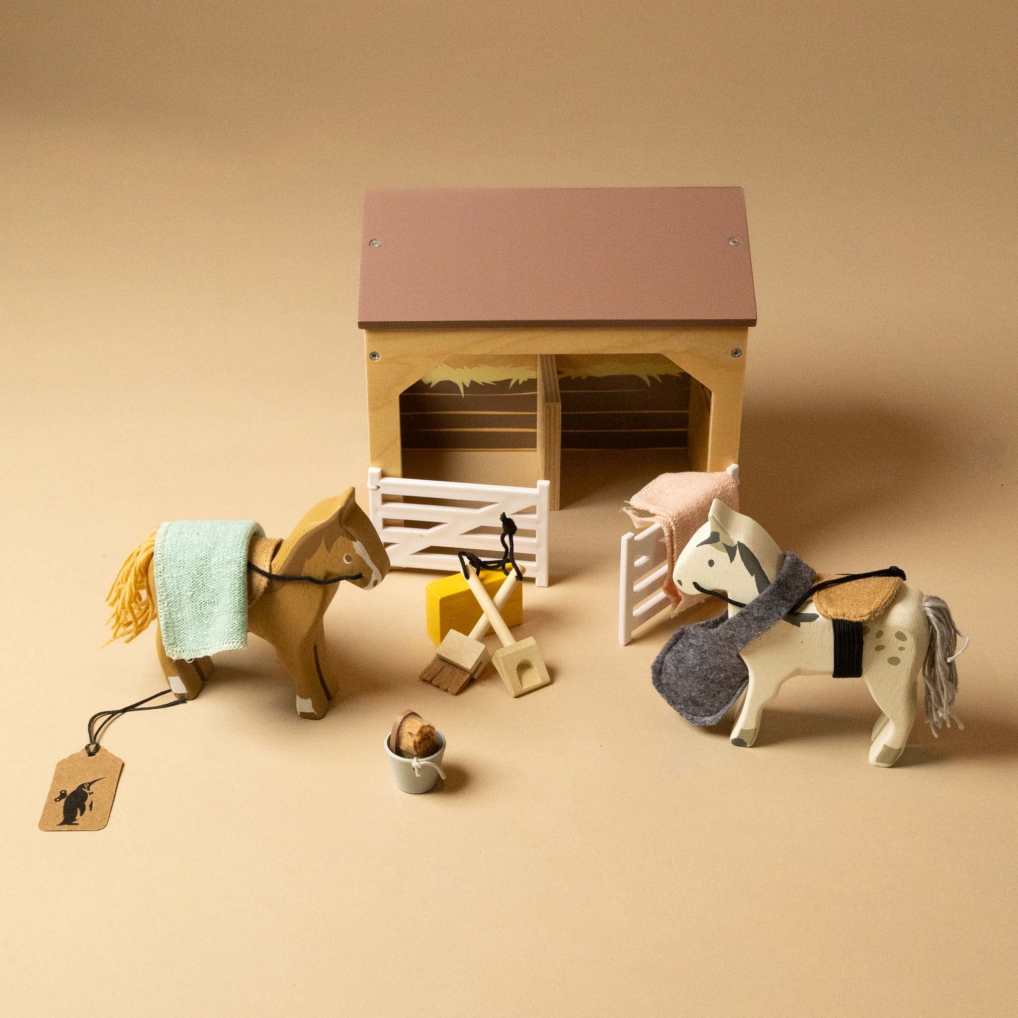 Toy horses and wooden-stable-play-set on a beige background