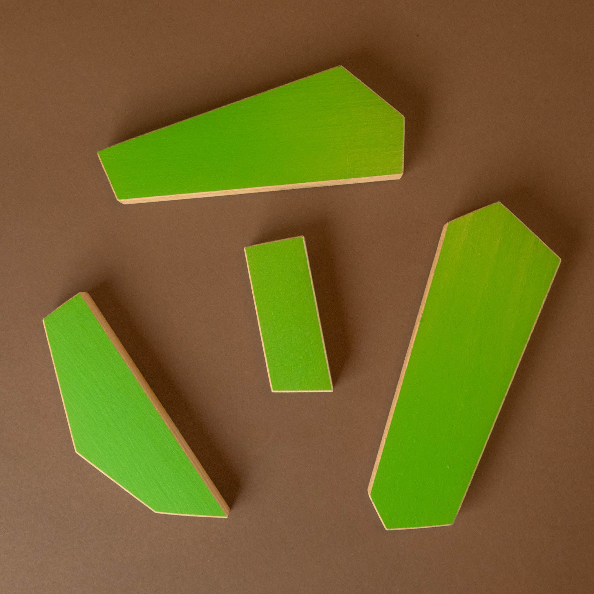 Four bright lime green geometric wooden blocks of different shapes arranged on a solid brown background.