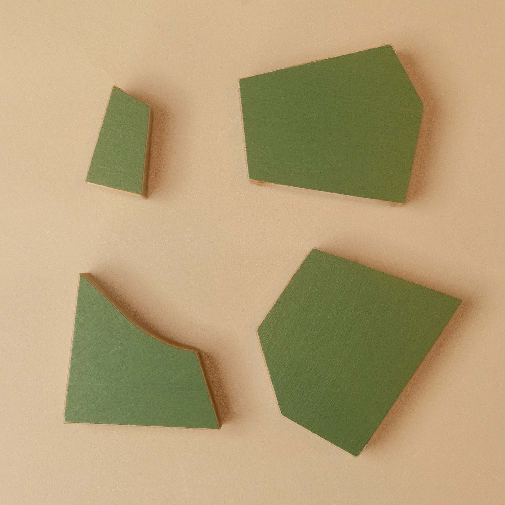 wooden-tree-poplar Four green geometric wooden blocks of different shapes arranged on a light beige background.